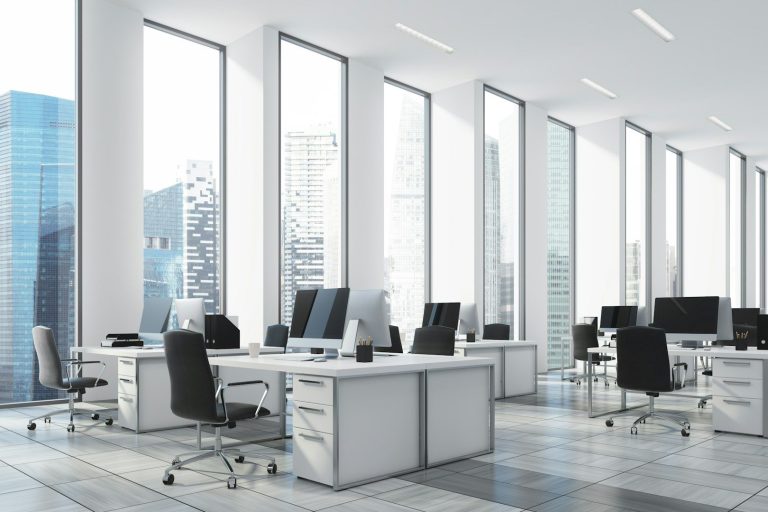 Moderne Büroumgebung mit Schreibtischen, Computern und großen Fenstern.
